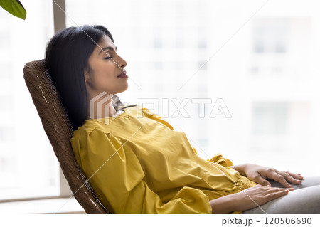 Calm sleepy beautiful young Indian woman resting on lounge chair 120506690