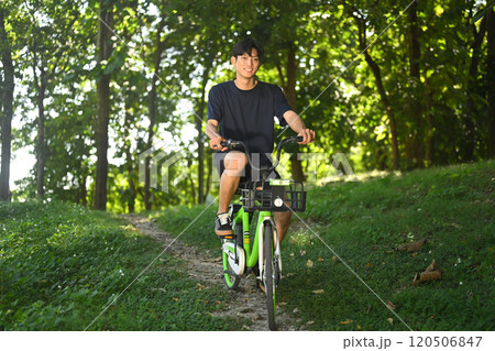 Young man riding a rental bike along a shaded dirt path surrounded by trees in a serene park Young man riding a rental bike along a shaded dirt path surrounded by trees in a serene park 120506847