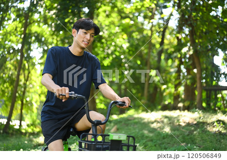 Young man riding a rental bike along a shaded dirt path surrounded by trees in a serene park Young man riding a rental bike along a shaded dirt path surrounded by trees in a serene park 120506849