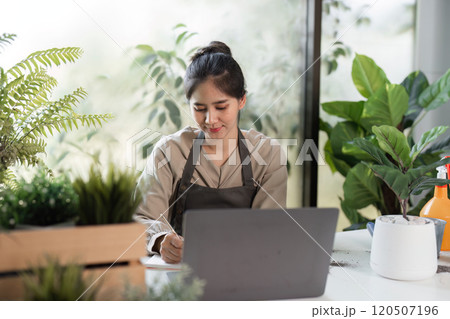 Woman Enjoying Indoor Gardening Surrounded by Lush Greenery and Modern Decor in a Sunlit Room 120507196