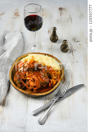 Beef stew with mashed potatoes, onions, and carrots on a white table, with red wine 120507777