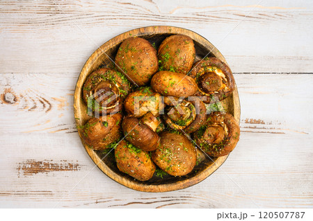 Deliciously baked mushrooms topped with herbs on a wooden plate in a rustic kitchen setting Deliciously baked mushrooms topped with herbs on a wooden plate in a rustic kitchen setting 120507787