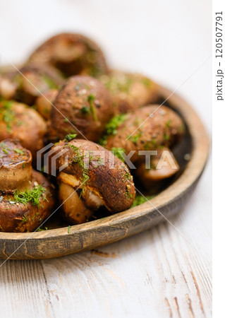 Close-up view of a freshly cooked mushrooms garnished with herbs on a rustic wooden platter 120507791