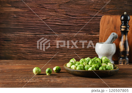 Fresh Brussels sprouts in a wooden bowl with kitchen tools against a rustic wooden backdrop 120507805