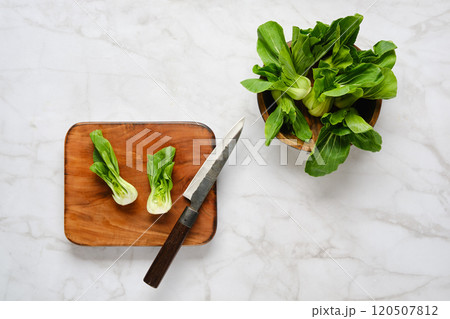 Preparing fresh bok choy on a wooden cutting board with a knife and additional greens nearby 120507812
