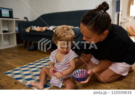 A mother lovingly assists her child in painting, creating cherished memories in a cozy home setting. The scene radiates warmth and creativity as they bond over a fun activity. A mother lovingly assists her child in painting, creating cherished memories in a cozy home setting. The scene radiates warmth and creativity as they bond over a fun activity. 120509638