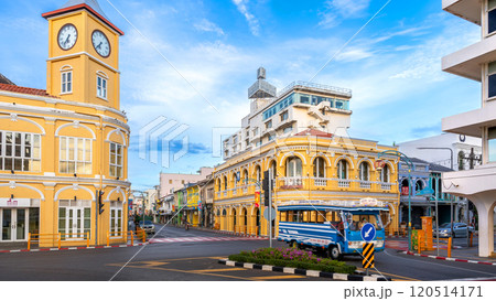 The iconic yellow clock tower and historic Chartered Bank building in Phuket Old Town, showcasing Sino-Portuguese architecture, frame a bustling intersection with a blue local bus passing by 120514171