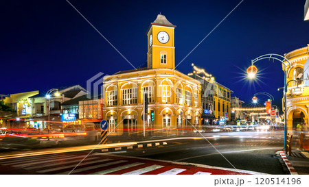 Night view of the Phuket Old Town Clock Tower illuminated with vibrant yellow lights, featuring bustling traffic light trails and cultural street decorations. Night view of the Phuket Old Town Clock Tower illuminated with vibrant yellow lights, featuring bustling traffic light trails and cultural street decorations. 120514196