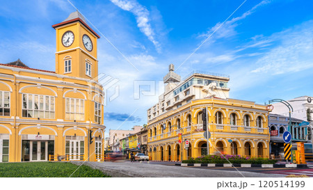 The historic Sino-Portuguese clock tower and Chartered Bank building in Phuket Old Town frame a bustling intersection, with a distinctive blue local bus passing under a clear blue sky The historic Sino-Portuguese clock tower and Chartered Bank building in Phuket Old Town frame a bustling intersection, with a distinctive blue local bus passing under a clear blue sky 120514199