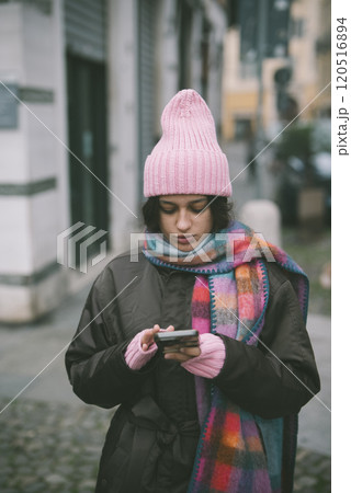 A woman in a pink hat and scarf is looking at her phone A woman in a pink hat and scarf is looking at her phone 120516894