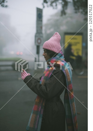 A woman, adorned in a pink hat and matching scarf, gazes at her phone A woman, adorned in a pink hat and matching scarf, gazes at her phone 120517022