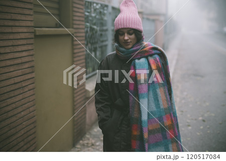 A woman in a pink hat and scarf stands on a foggy street A woman in a pink hat and scarf stands on a foggy street 120517084