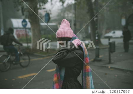 A woman is walking down the street, wearing a stylish pink hat and scarf A woman is walking down the street, wearing a stylish pink hat and scarf 120517097
