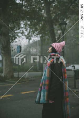 A woman in a pink hat and scarf stands on a foggy street 120517105