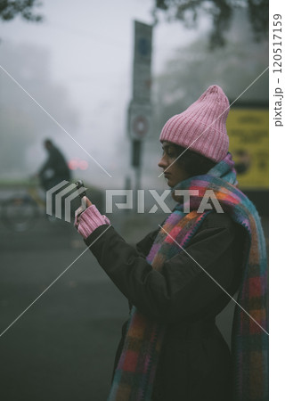 A woman in a pink hat and scarf is intently looking at her phone 120517159