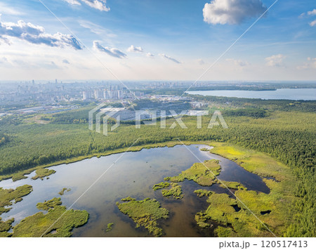 Big lake with green shores in bright sun light and city on horizon, aerial landscape. Recreation concept. Aerial view 120517413