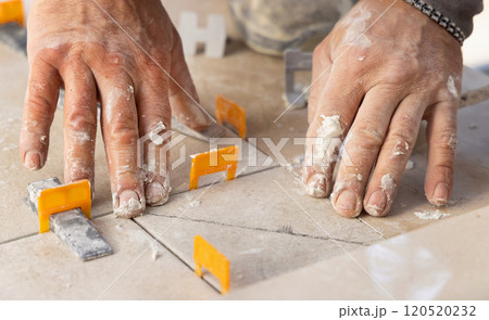 Tiler laying the ceramic tile on the floor with dusty hands. Home renovation or building new house 120520232