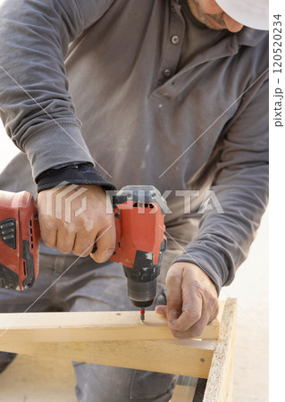 Carpenter working on wooden board using professional electric cordless screwdriver 120520234
