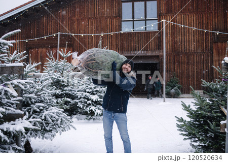 Handsome bearded man holding wrapped Christmas tree on fair. Happy male bring fir tree. 120520634