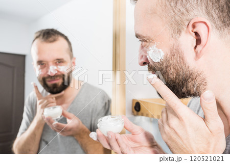 Man applying moisturizer cream in bathroom Man applying moisturizer cream in bathroom 120521021