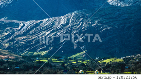 A breathtaking view features a dramatic mountain range with steep slopes and vibrant green fields nestled below. The scene is illuminated by the soft glow of morning sunlight. A breathtaking view features a dramatic mountain range with steep slopes and vibrant green fields nestled below. The scene is illuminated by the soft glow of morning sunlight. 120521256