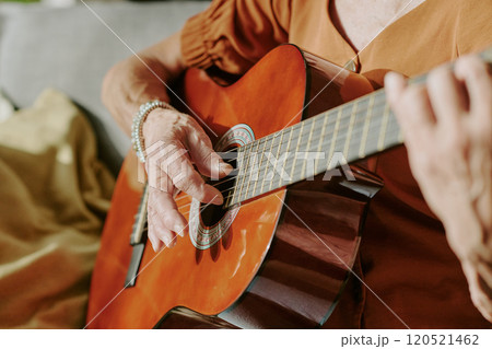 Elderly person skillfully strumming an acoustic guitar, creating melodious tunes that resonate in a cozy living room setting 120521462