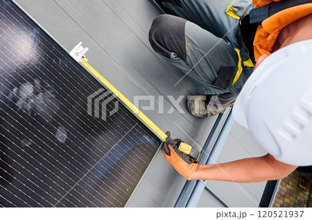 Worker building solar panel system on rooftop of house for generating electricity through photovoltaic effect. Close up man using ruler to measure mounting equipment for precise installation. Worker building solar panel system on rooftop of house for generating electricity through photovoltaic effect. Close up man using ruler to measure mounting equipment for precise installation. 120521937