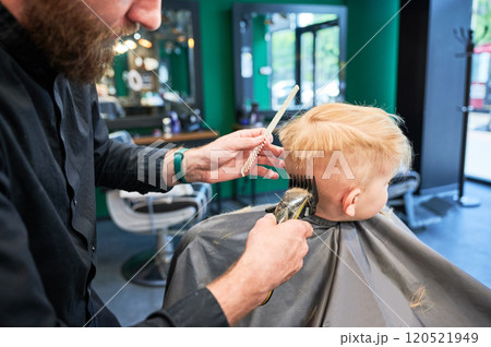 Back view of hairdresser shaving boy's head. Adorable boy getting stylish haircut. Blond kid in beauty salon. 120521949