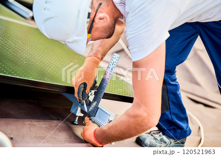 Worker building solar panel system on rooftop of house for generating electricity through photovoltaic effect. Close up man using ruler to measure mounting equipment for precise installation. Worker building solar panel system on rooftop of house for generating electricity through photovoltaic effect. Close up man using ruler to measure mounting equipment for precise installation. 120521963