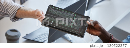 Close-up of two professionals exchanging tablet displaying code in an office environment There is emphasis on collaborative effort in a tech-related project 120522277