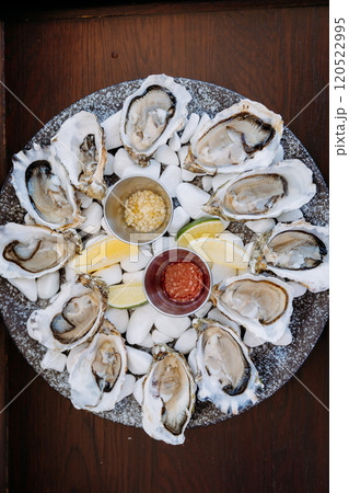 Fresh oysters on ice with lemon wedges and sauces, served elegantly for a seafood dining experience Fresh oysters on ice with lemon wedges and sauces, served elegantly for a seafood dining experience 120522995