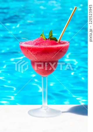 Chilled red drink on pool edge in bright sunlight. Concept of tropical refreshment and summer leisure Chilled red drink on pool edge in bright sunlight. Concept of tropical refreshment and summer leisure 120523945