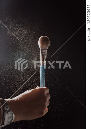 Powder brush in dramatic lighting with floating particles, beauty and makeup artistry in action 120523983