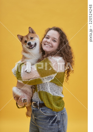 Vertical portrait of joyful young woman holding cute red Shiba Inu dog while posing together with pet friend against yellow background in studio, copy space Vertical portrait of joyful young woman holding cute red Shiba Inu dog while posing together with pet friend against yellow background in studio, copy space 120524248