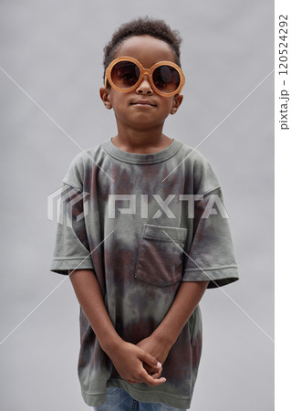 Vertical studio shot of stylish little Black boy wearing gray t shirt paired with colorful sunglasses posing in studio against blurred background 120524292