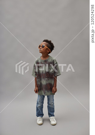 Vertical shot of little Black boy in casual outfit and stylish sunglasses looking away while standing against gray background in studio, copy space Vertical shot of little Black boy in casual outfit and stylish sunglasses looking away while standing against gray background in studio, copy space 120524298