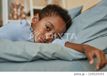 Portrait shot of little Black boy lying in bed waking up after long healthy sleep on weekend morning in kids room, copy space 120524341