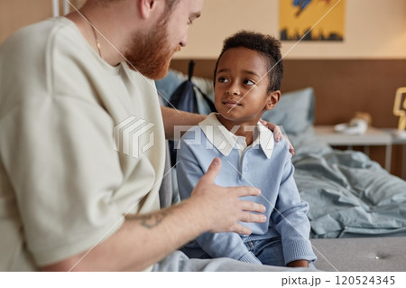 Medium shot of little Black boy listening with attention to supportive adoptive father during important conversation while sitting on bed in kids room, copy space Medium shot of little Black boy listening with attention to supportive adoptive father during important conversation while sitting on bed in kids room, copy space 120524345