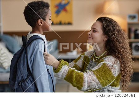 Side view of happy adoptive mother adjusting sons clothes while preparing little Black boy for school in kids room 120524361