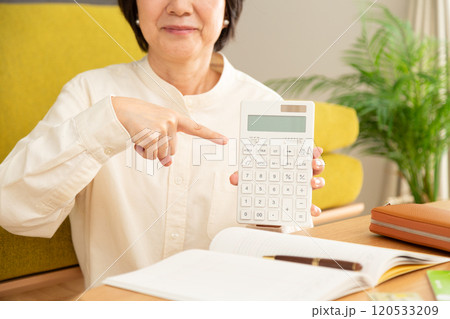 電卓を笑顔で指差すミドル女性と家計簿 120533209