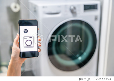 Young woman using mobile phone control via wi-fi and app for washing machine in home. Homesmart and new technology concept Young woman using mobile phone control via wi-fi and app for washing machine in home. Homesmart and new technology concept 120535593