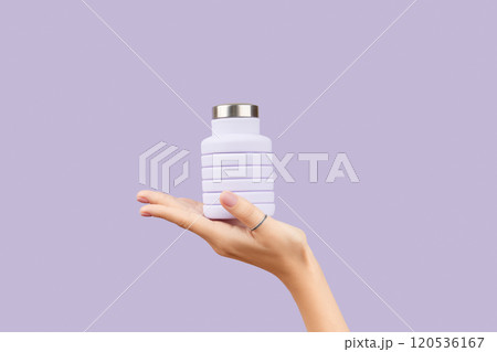 Womans hand holding collapsible reusable lilac water bottle on purple background. Zero waste Womans hand holding collapsible reusable lilac water bottle on purple background. Zero waste 120536167