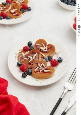 A heap of heart shaped pancakes with berries and cutlery on the white plate on grey background A heap of heart shaped pancakes with berries and cutlery on the white plate on grey background 120536177