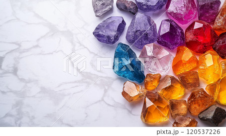 A collection of purple, orange, and blue gemstones with luminous surfaces on a light marble background A collection of purple, orange, and blue gemstones with luminous surfaces on a light marble background 120537226