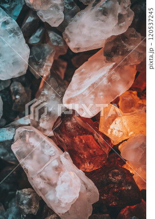 Closeup of raw, glowing crystals in icy blue, amber, and red tones illuminated with warm light 120537245