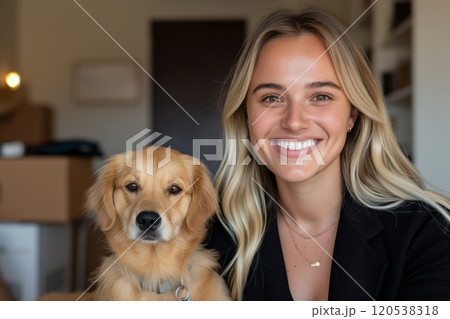 A smiling woman sits beside her dog, surrounded by cardboard boxes in a cozy room 120538318