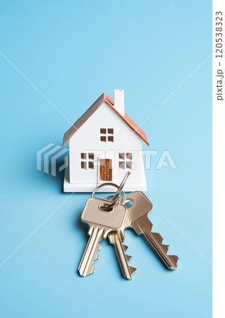 Miniature house model with three metal keys placed in front, set against a clean blue backdrop 120538323