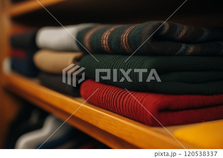 A row of folded sweaters in green, red, and brown with stripe patterns, neatly arranged on a shelf 120538337
