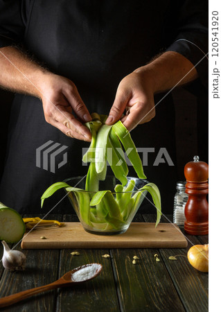 A chef fills a glass bowl with chopped vegetable marrow before cooking. Concept of preparing zucchini for a vegetable dinner 120541920