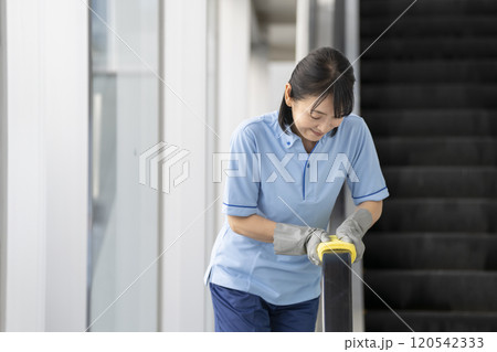 エスカレーターの手すりを拭くミドルの女性清掃スタッフ 120542333